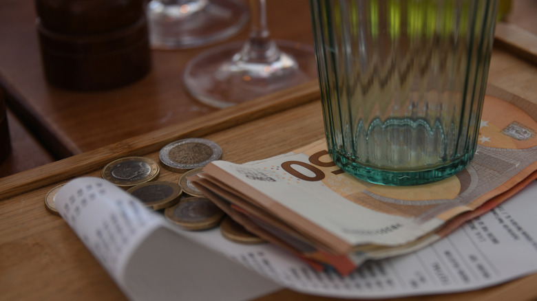 Du papier-monnaie, des pièces de monnaie et un reçu papier sous un verre vide.