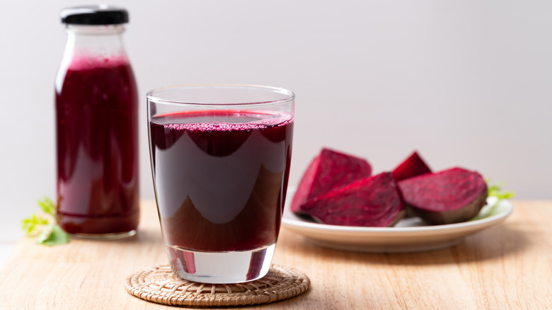 Concentrez-vous sur un verre de jus de betterave avec une bouteille et des tranches de betterave en arrière-plan