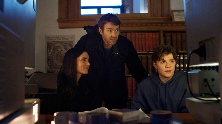 Joel Edgerton dans le rôle de Jason Dessen debout derrière Jennifer Connelly dans le rôle de Daniela Dessen et Oakes Fegley dans le rôle de Charlie Dessen dans une bibliothèque de Dark Matter