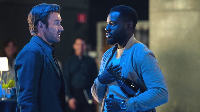 Joel Edgerton dans le rôle de Jason2 debout à côté de Dayo Okeniyi dans le rôle de Leighton Vance alors qu'il tient deux bouteilles de champagne dans Dark Matter