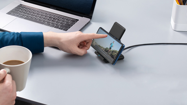 Personne utilisant un téléphone pendant qu'il est en train de charger sur un support de chargement sans fil.
