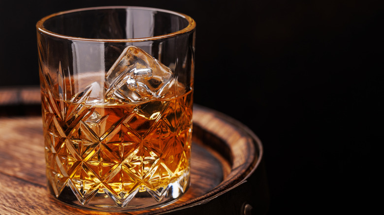 Verre de whisky avec de la glace posé sur un tonneau en bois