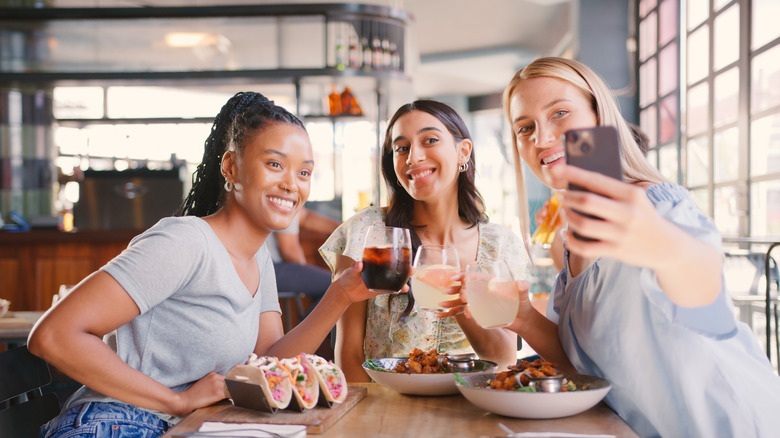 Groupe d'amies posant avec des boissons et de la nourriture à une table de restaurant