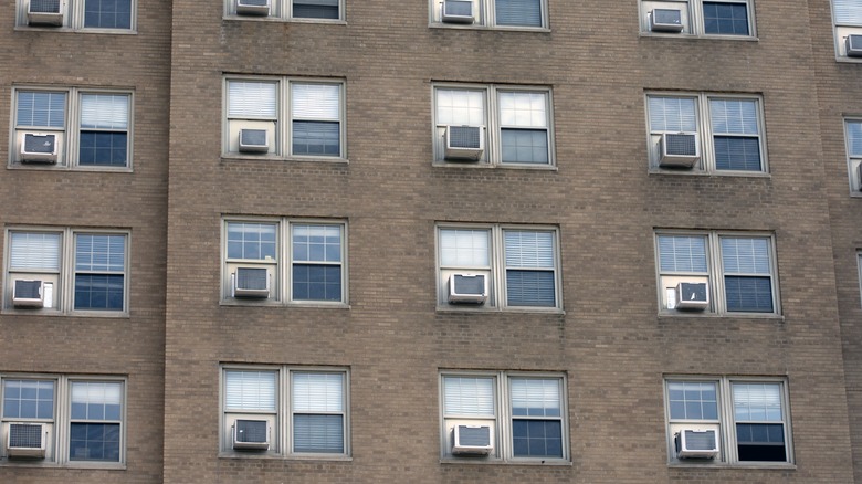 Une variété de climatiseurs de fenêtre dans un immeuble multifamilial vu de l’extérieur.
