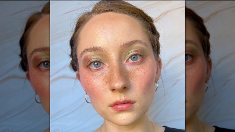 Une personne avec des taches de rousseur et un maquillage radieux pour les yeux posant pour une photo