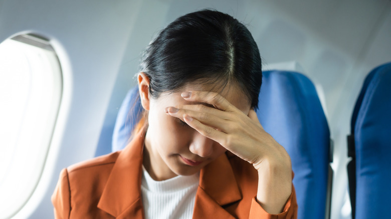 Une passagère d'avion, la tête baissée et la main cachant son visage, embarrassée