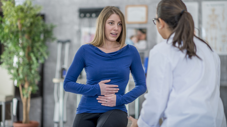 Femme tenant son ventre tout en parlant avec un médecin