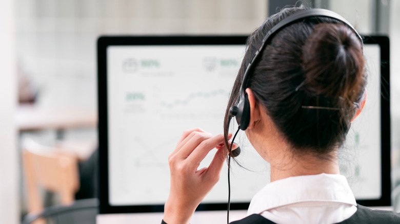 photo d'une femme de dos à un bureau devant un ordinateur portant un casque avec un microphone pour le service client