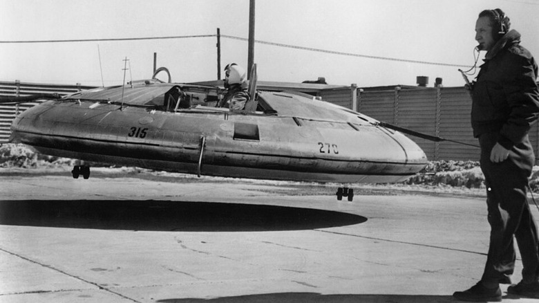 Le pilote d'un engin en forme de soucoupe volante Avrocar s'élève au-dessus du sol avec un léger angle