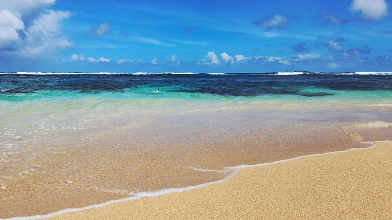 Plage de sable doré au premier plan avec une mer turquoise s'assombrissant jusqu'à un bleu profond en arrière-plan