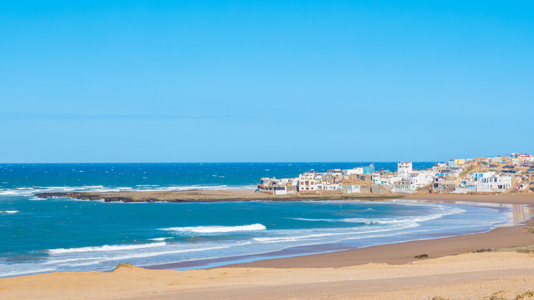 Courbe de plage dorée contre la mer bleue avec village blanc en arrière-plan