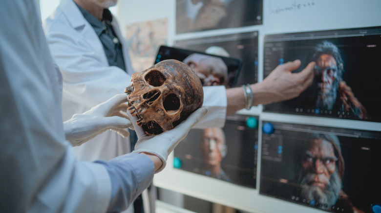 Scientifique tenant un crâne humain fossilisé devant des écrans d'anciens visages humains CGI