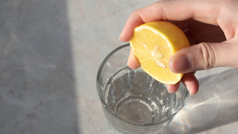 Gros plan d'une main pressant la moitié d'un citron sur un verre d'eau.