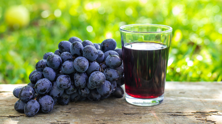 grappe de raisins rouges avec un verre de jus de raisin rouge à côté d'eux