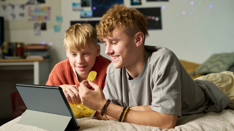 Adolescent souriant et son jeune frère mangeant des chips et regardant un ordinateur portable