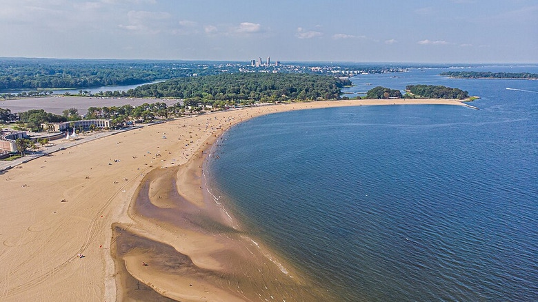 Vue aérienne d'Orchard Beach en forme de croissant, avec forêt et bâtiments en arrière-plan