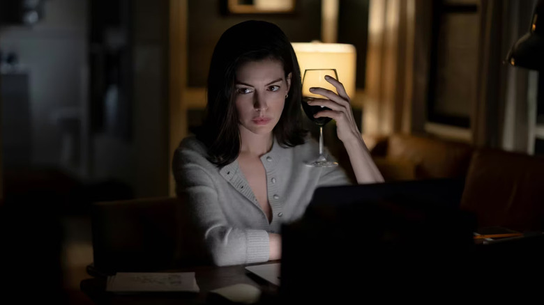 Verity écrit sur son ordinateur portable et tient un verre de vin dans Verity