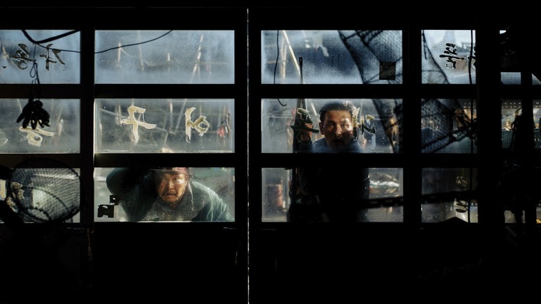 Hwang Jung-min dans le rôle de Bum-seok tenant une arme et regardant à travers une fenêtre de garage dans Hope