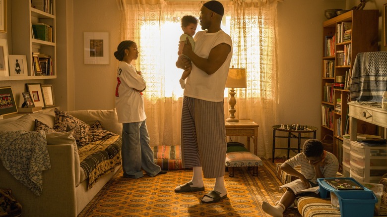 Mahershala Ali dans le rôle de Latif tenant un bébé et debout dans son salon à côté d'Adia dans le rôle de Fatiha et Jahleel Kamara dans le rôle de Qadir dans Your Mother Your Mother Your Mother