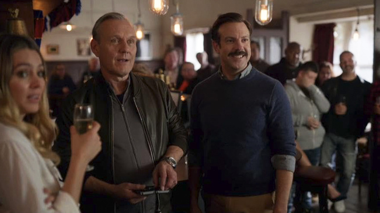 Rupert, Ted et Bex se tiennent côte à côte dans le pub de Mae à Ted Lasso