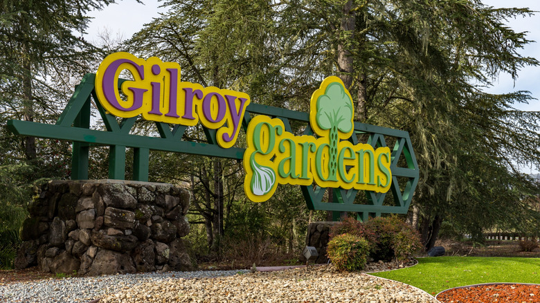 Un panneau Gilroy Gardens à l'extérieur du parc à thème, avec de l'herbe verte et des arbres en arrière-plan
