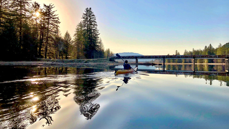 Un homme faisant du kayak à l'heure d'or vers un pont sur un lac près de Petersburg, en Alaska