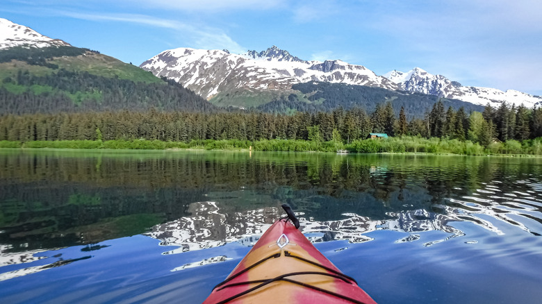 L'avant d'un kayak rouge sur un lac immaculé entouré de forêt et de sommets enneigés près de Seward, en Alaska