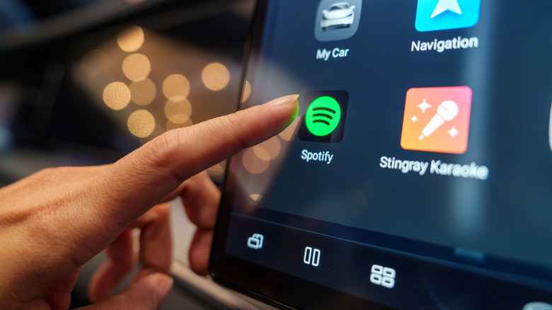 Un gros plan d'un doigt est sur le point d'appuyer sur l'icône Spotify sur l'écran d'une voiture