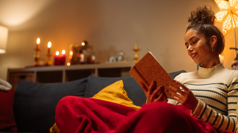 Jeune femme souriante en lisant un livre avec des bougies allumées en arrière-plan