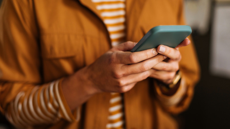 gros plan d'une personne qui garde une orange brûlée à l'aide d'un smartphone