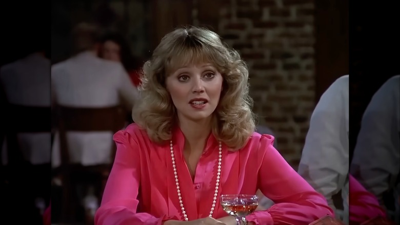 Shelley Long porte un chemisier rose vif et un long collier de perles