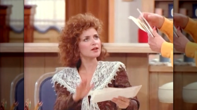 Annie Potts portant un chemisier marron bordé de dentelle avec des cheveux roux bouclés