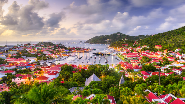 Des yachts flottent dans le port de Saint-Barthélemy à l'heure d'or, entourés de maisons aux toits rouges
