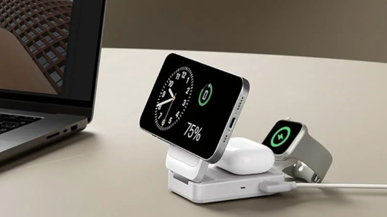 Une station de recharge sans fil Anker blanche installée à proximité d'un ordinateur portable et chargeant un téléphone, des écouteurs et une montre