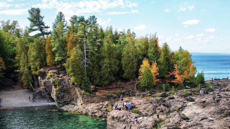 Les gens explorent un rivage rocheux avec des conifères et un feuillage automnal sur les eaux turquoise du lac Supérieur, dans le parc national de l'Isle Royale