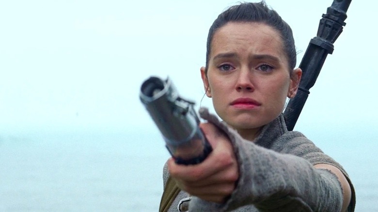 Daisy Ridley dans le rôle de Rey tend un sabre laser dans Star Wars : Épisode VII – Le Réveil de la Force