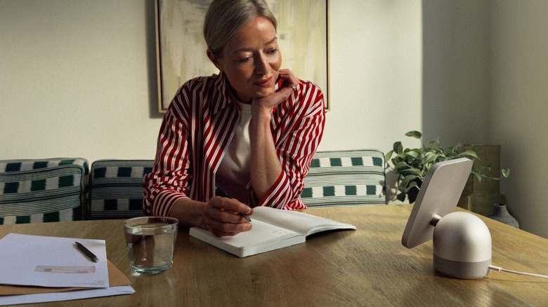 Une femme lit depuis un appareil Apple HomeView sur une table.