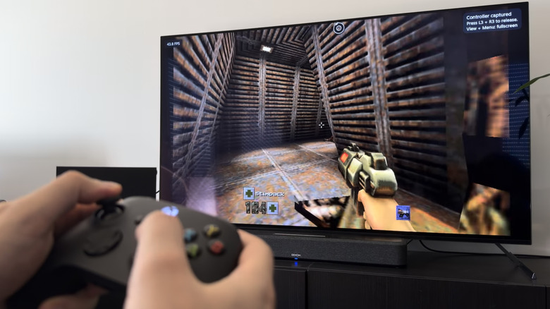 Une main tenant une manette Xbox noire devant un téléviseur exécutant Quake