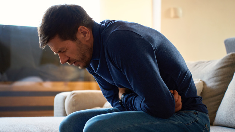 Homme assis sur un canapé et se penchant en avant avec les bras sur le ventre