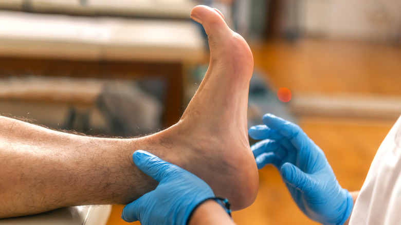 Un professionnel de la santé portant des gants bleus examine le pied d'un patient