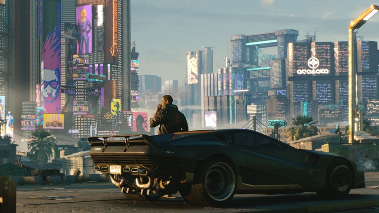Gavin Drea dans le rôle de la voix de V appuyé contre sa voiture sur une route surplombant Night City dans Cyberpunk 2077