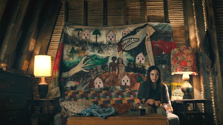 Julie Matthews de Hannah Cheramy est assise devant une tapisserie montrant une ville menacée par des créatures dans From