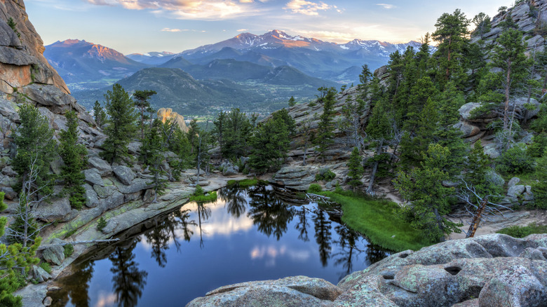 Lac alpin dans le parc national des Montagnes Rocheuses entouré de rochers et d'arbres à feuilles persistantes avec des montagnes au loin