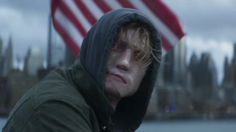 Matt Hagen/Clayface de Tom Rhys Harries assis au bord d'une rivière devant un drapeau américain à Clayface