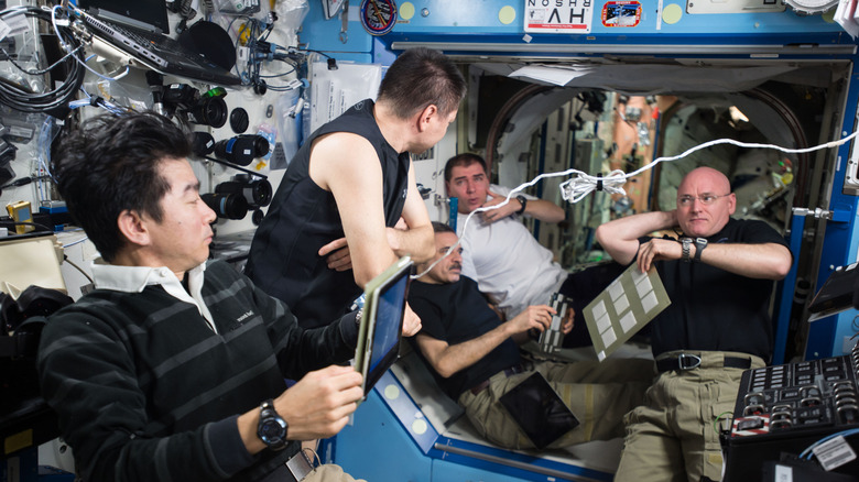 cinq astronautes masculins sur l'ISS en discussion entourés d'équipement