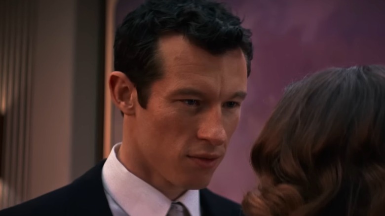 Callum Turner dans le rôle de Luke portant un costume et une cravate et regardant attentivement Elizabeth Olsen dans le rôle de Joan in Eternity