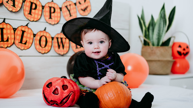 Un bébé en costume de sorcière avec un décor de citrouille.
