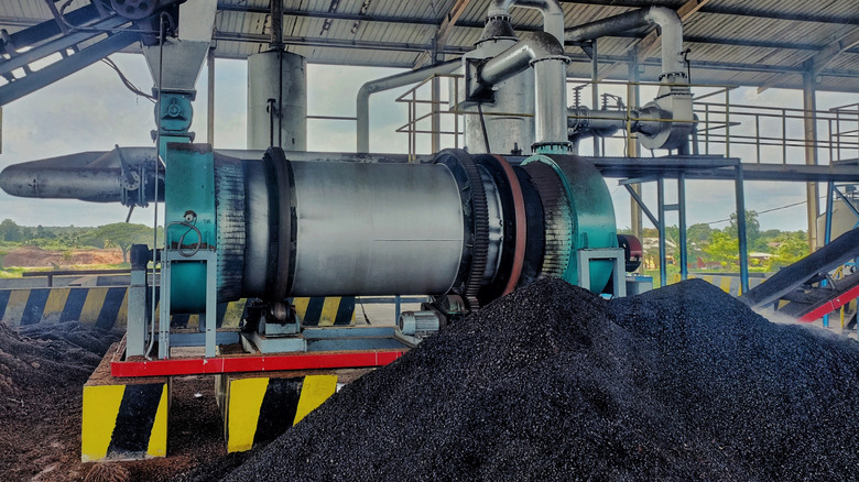 Un tas de biochar noir devant les machines de production