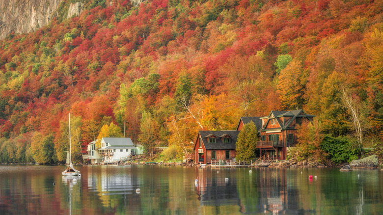 Une cabane au bord du lac Willoughby entourée de feuilles d'automne et d'un voilier sur l'eau