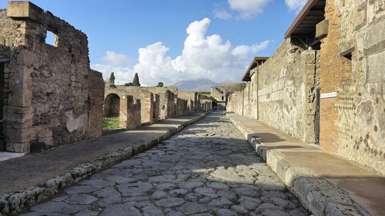 Une rue pavée parmi les ruines de Pompéi, en Italie, avec le Vésuve en arrière-plan